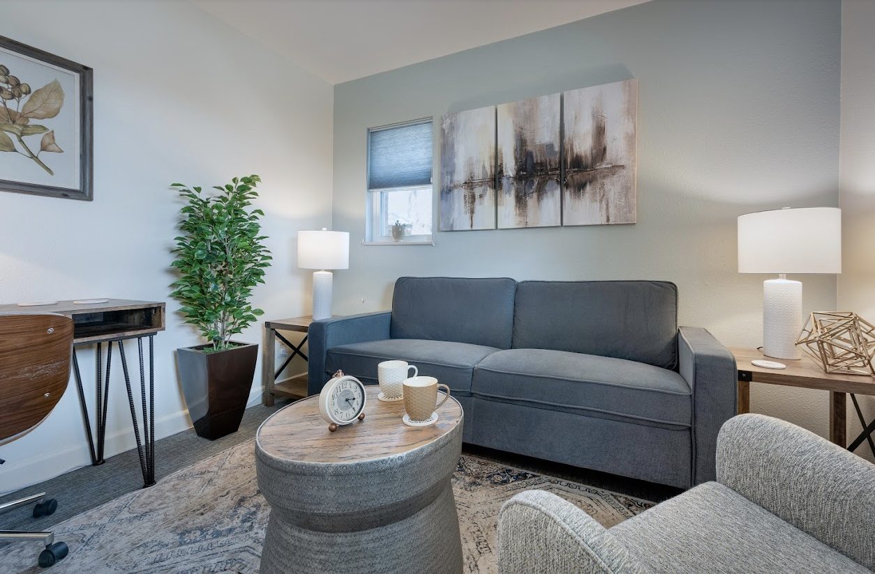 The office: a gray sofa, armchair, and round table with soft lamplight